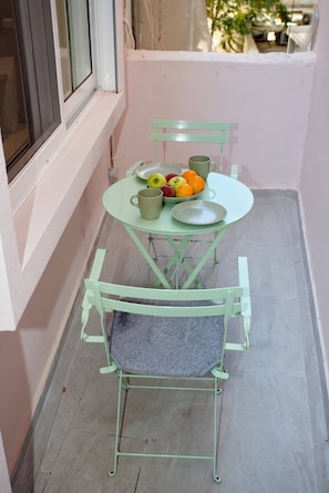 Un petit balcon avec une table et des chaises, un saladier rempli de fruits et une tasse.