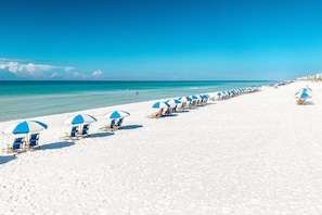 Una playa con hileras de sombrillas azules y blancas y sillas de playa.