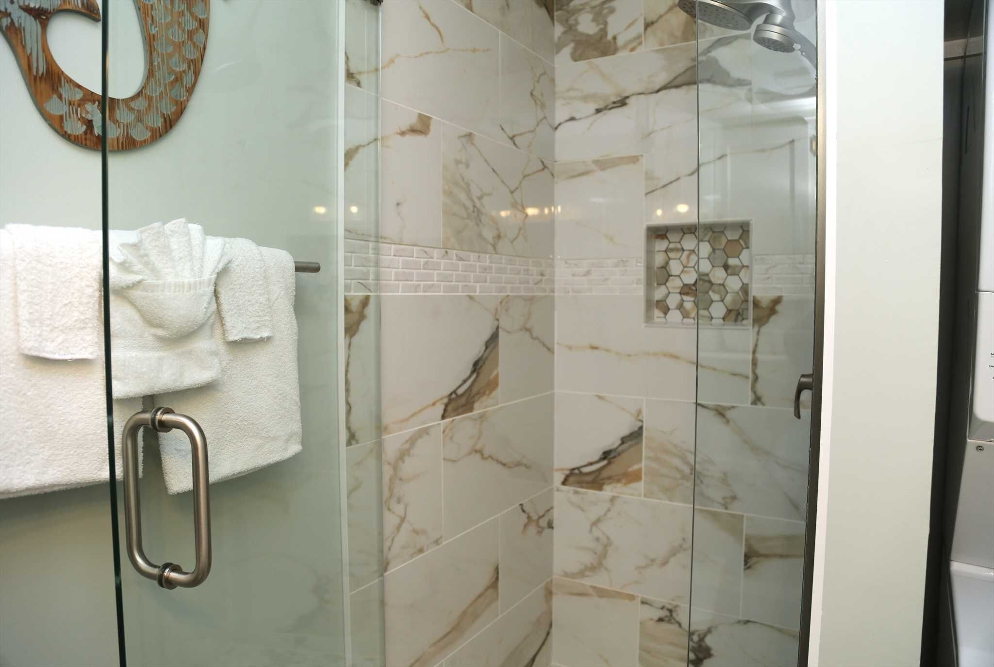 A glass-enclosed shower with marble tiles and a towel rack with white towels.