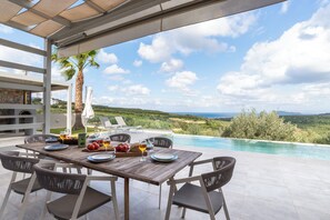 Mesa de madera preparada para una comida con vista a una piscina y al paisaje.