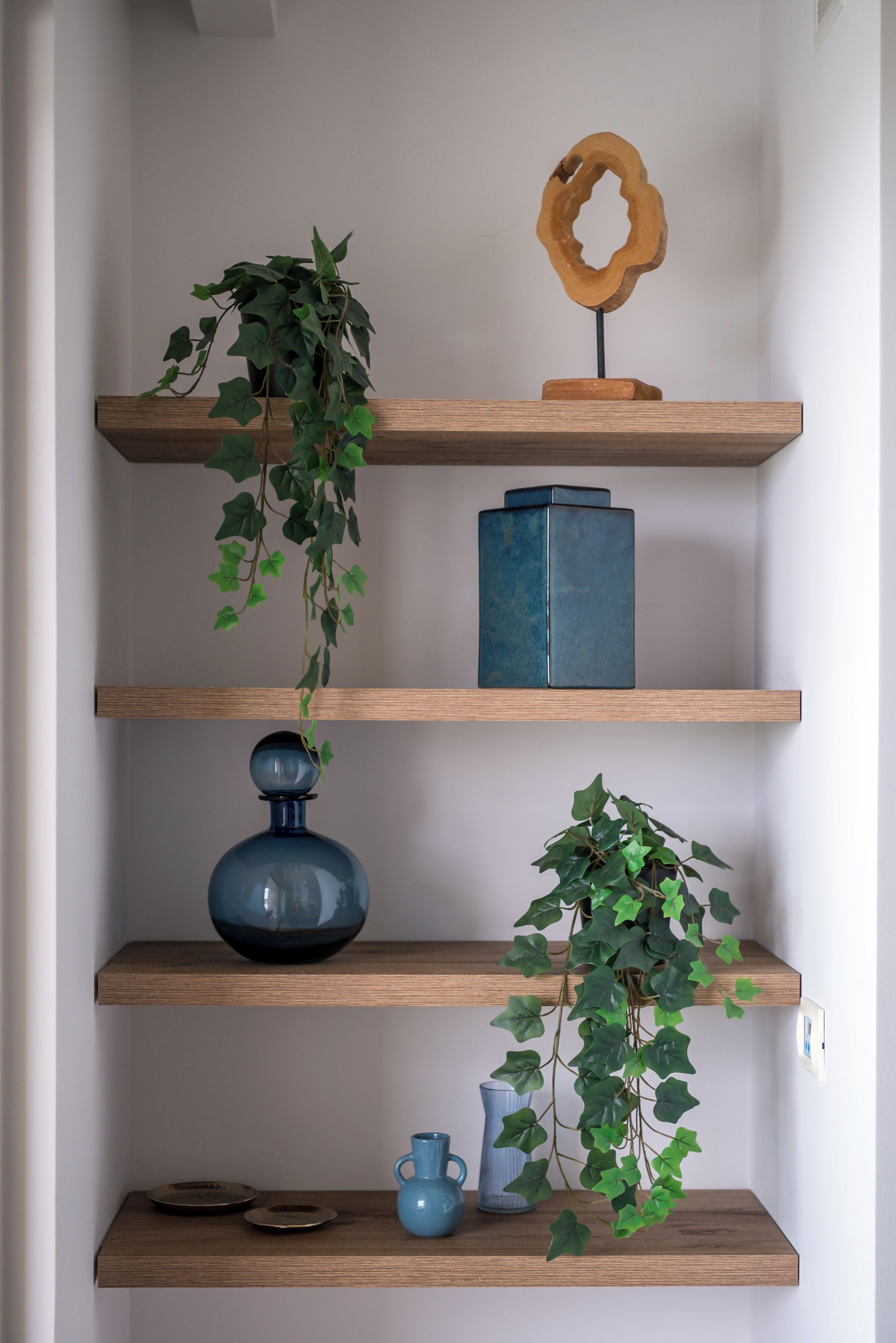 A wooden shelving unit with various decorative items including a vase, a bowl, and a hanging plant.