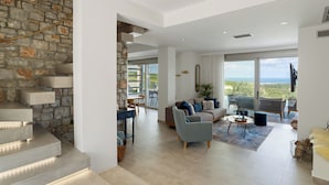 A modern living room with a stone wall, a staircase, a sofa set, and a view of the outdoors. - Villa Chryso (Platanias)