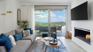 A modern living room with a sofa, coffee table, and fireplace. There is a sliding glass door leading to a balcony with outdoor furniture. - Villa Chryso (Platanias)