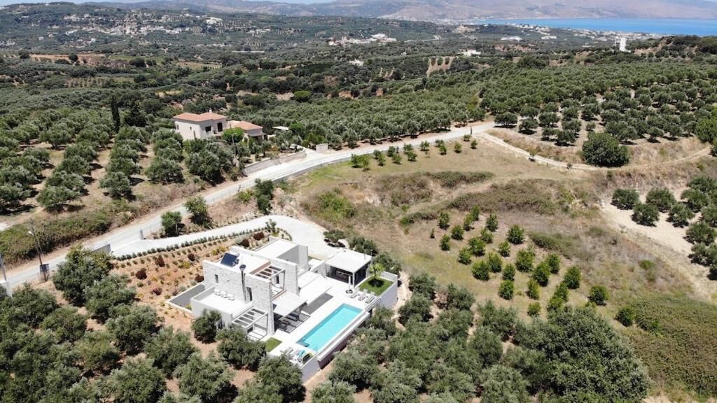 Vista aérea de una propiedad con una casa moderna, piscina y olivares circundantes.
