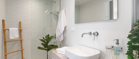 A modern bathroom with a white sink, a large mirror, and a glass-enclosed shower.