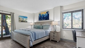 Una camera da letto con un letto in legno, una scrivania e una sedia. Sono presenti due finestre con persiane e un quadro appeso al muro.