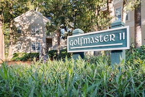 Ein Schild mit der Aufschrift 'golfmaster II' in einer üppigen, grünen Umgebung, im Hintergrund ein Gebäude.