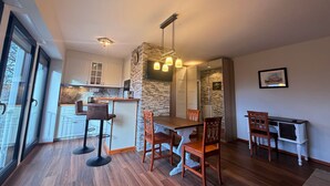 A modern kitchen with white cabinets, a stone accent wall, and a dining area with wooden chairs and a table. - Fully furnished flat in a lovely villa (Bergisch Gladbach)