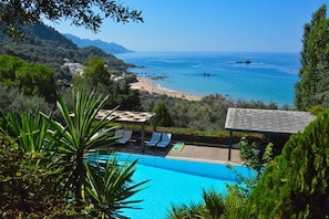 A pool with lounge chairs, a view of the sea, and a mountainous landscape. - Hippo One Bedroom Apartment (Pelekas)