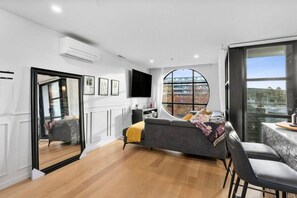 A modern living room with a grey sofa, a round window, and a city view. - Chic Braddon Branx Apartment Near Cafés & CBD (Braddon)