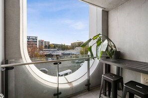 A balcony with a view of a cityscape, a potted plant, and a small table with two stools. - Chic Braddon Branx Apartment Near Cafés & CBD (Braddon)