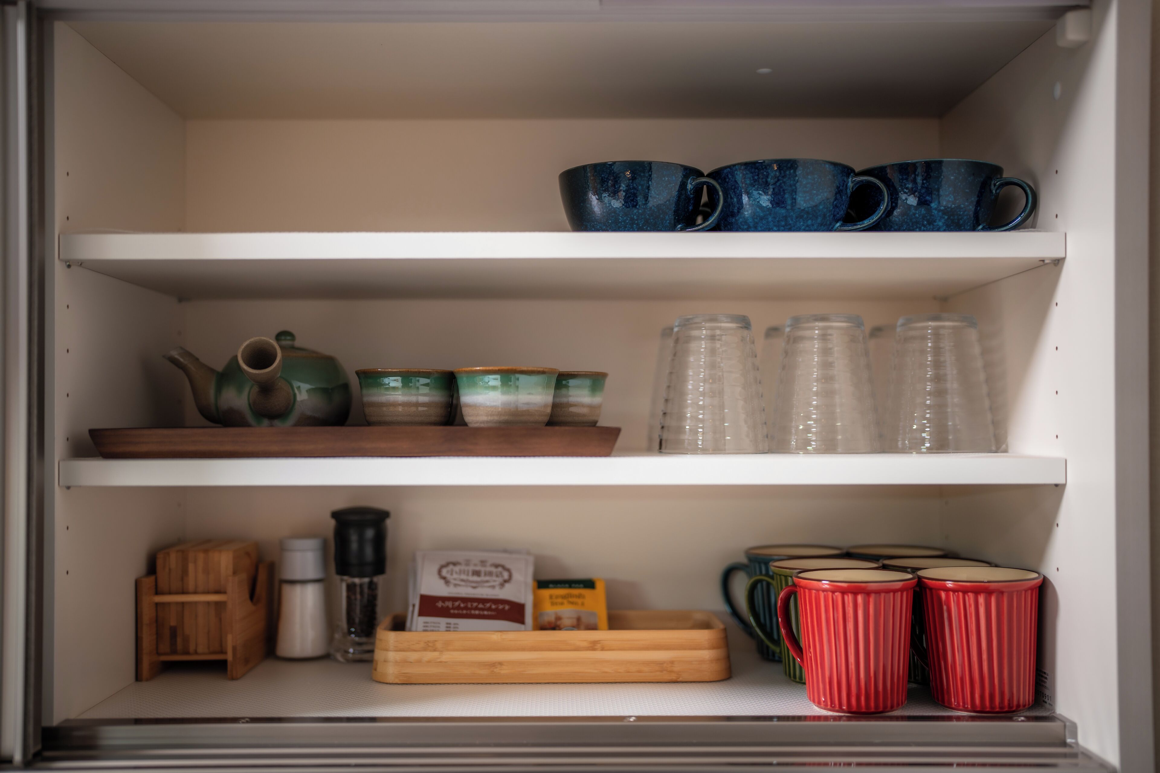 A kitchen with shelves holding various kitchenware, including cups, bowls, and a kettle.