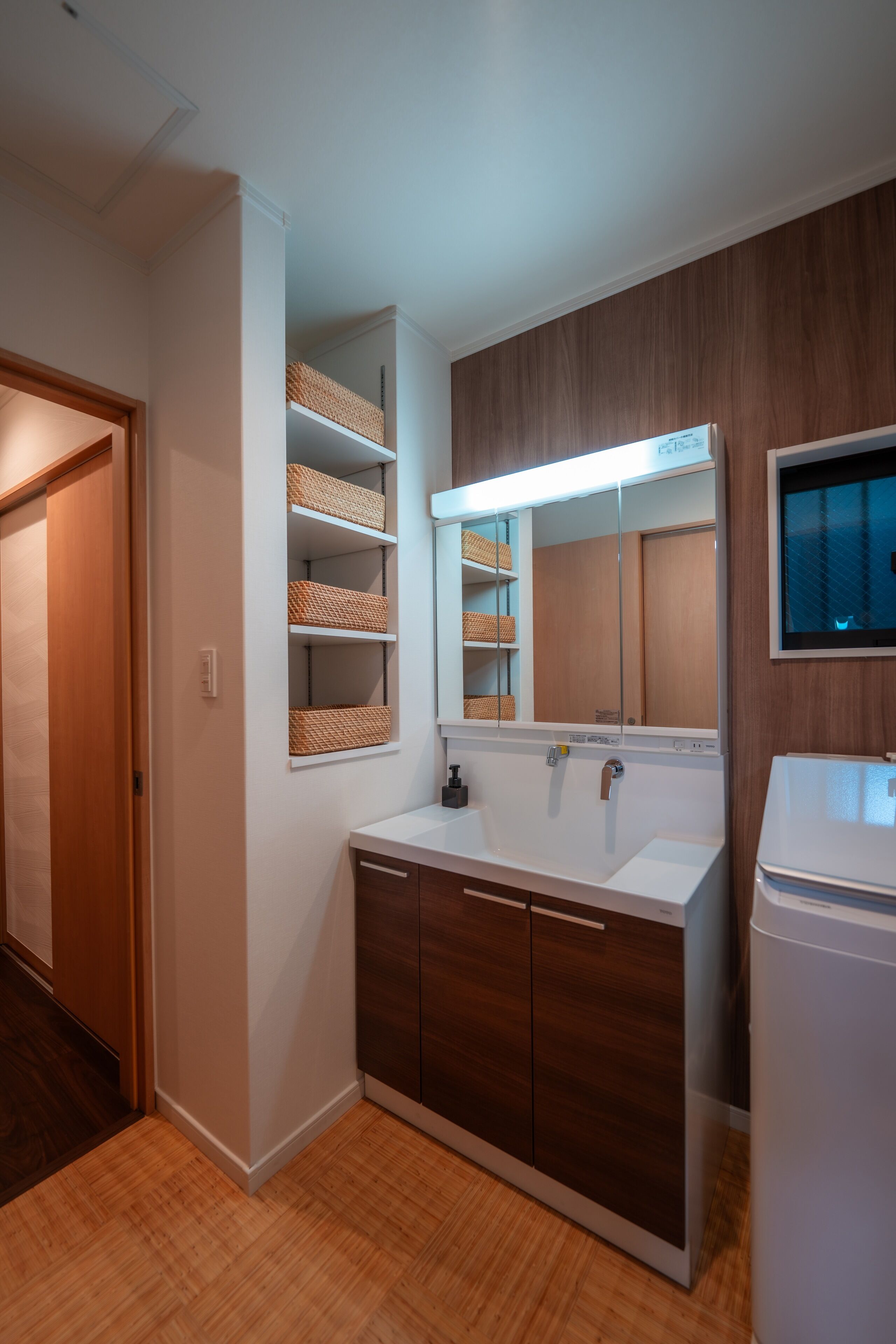 A bathroom with a wooden vanity, a large mirror, and wicker baskets on shelves.