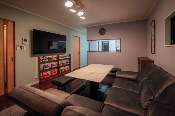 A modern living room with a flat-screen TV, a wooden bookshelf, a dining table, and a sofa. - Private Residence Kyoto Station North (Kyoto)