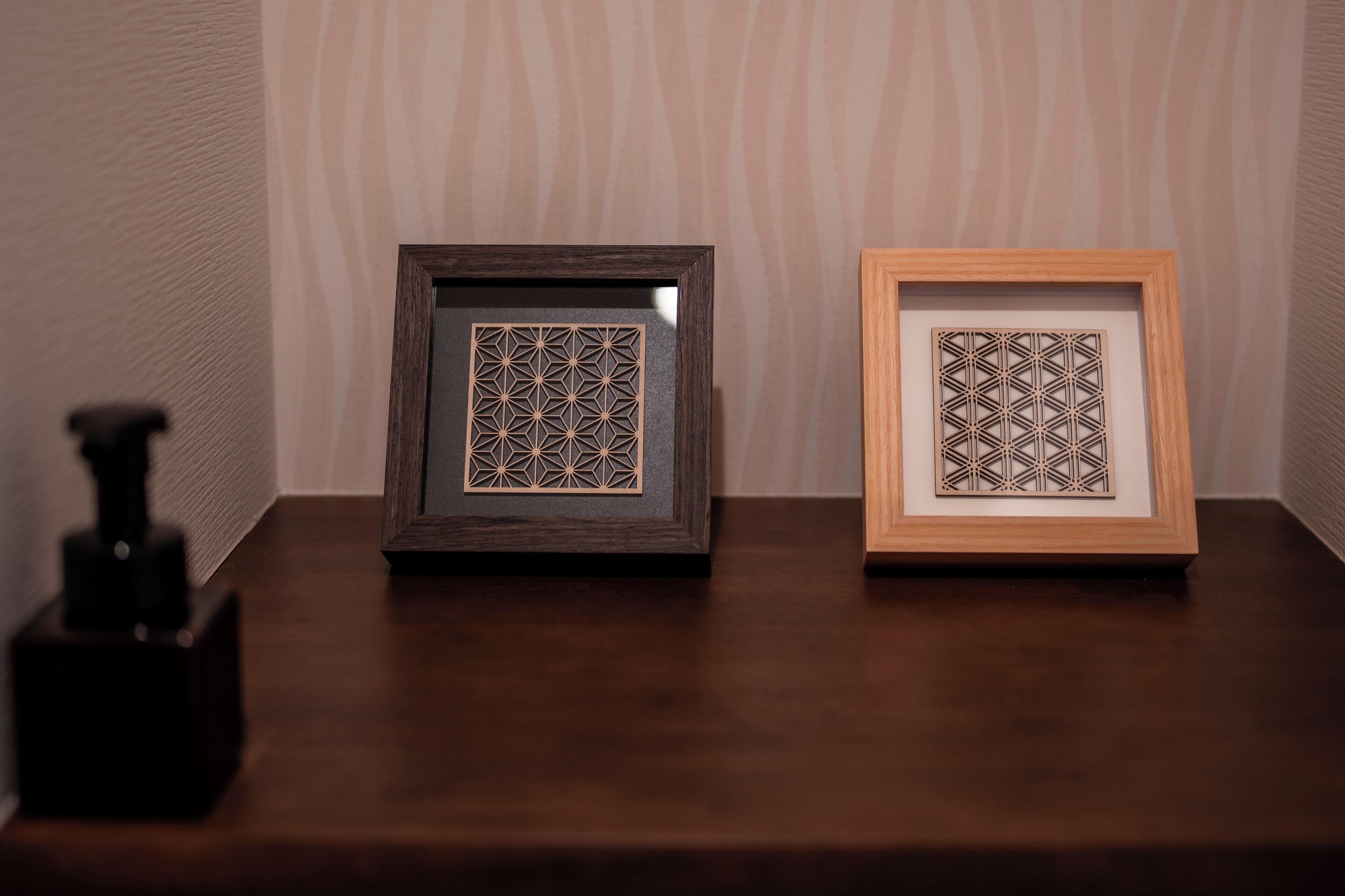 Two framed geometric patterns on a wooden table against a striped wallpaper background.