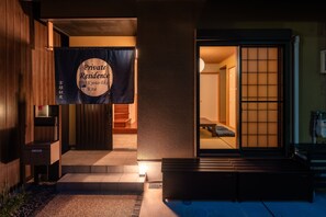 Entrada de una residencia privada con puerta corrediza, un pequeño espacio exterior con asientos y un cartel que indica la ubicación en Kioto, Japón.
