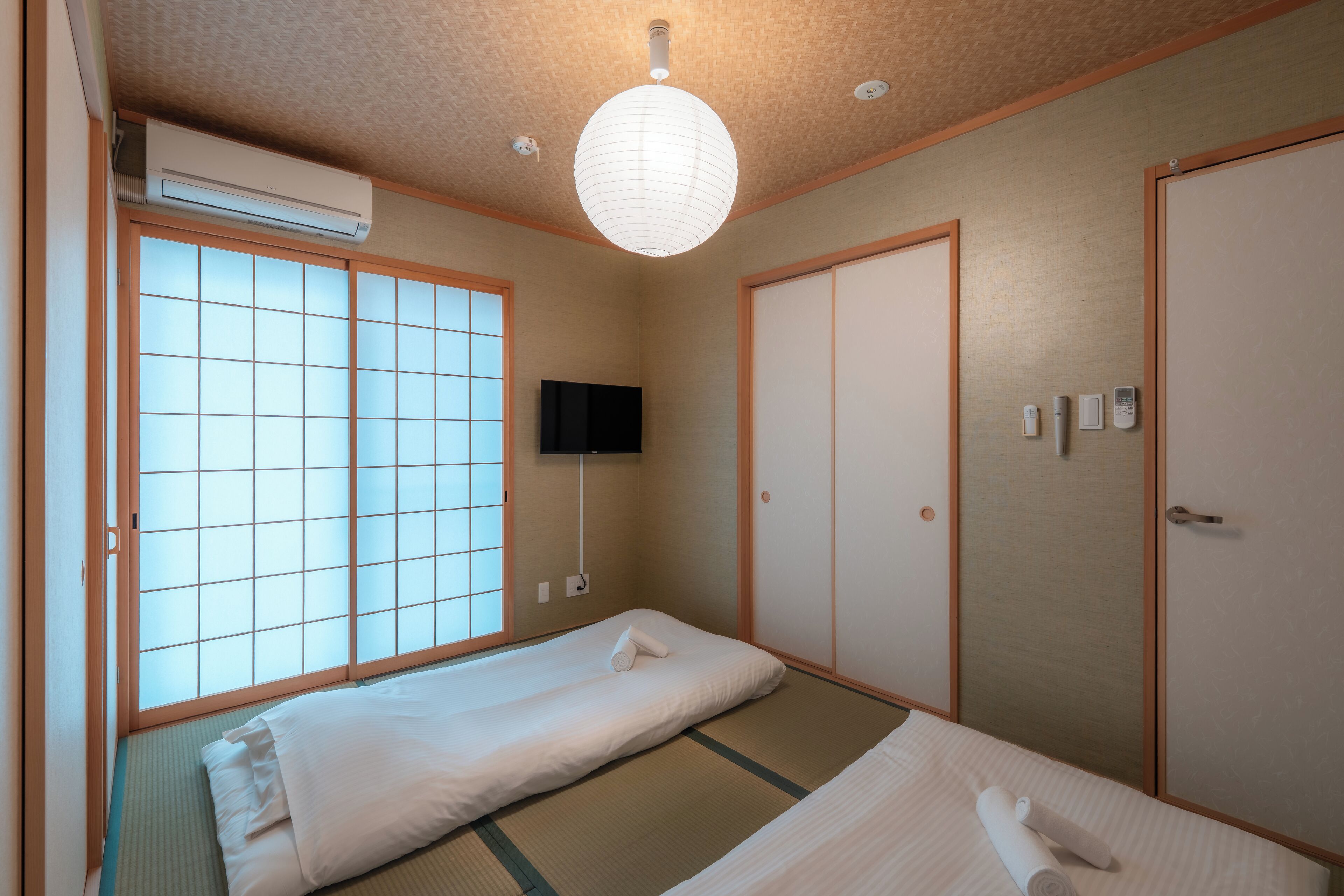 A traditional Japanese room with tatami flooring, a futon bed, sliding doors, and a mounted TV.