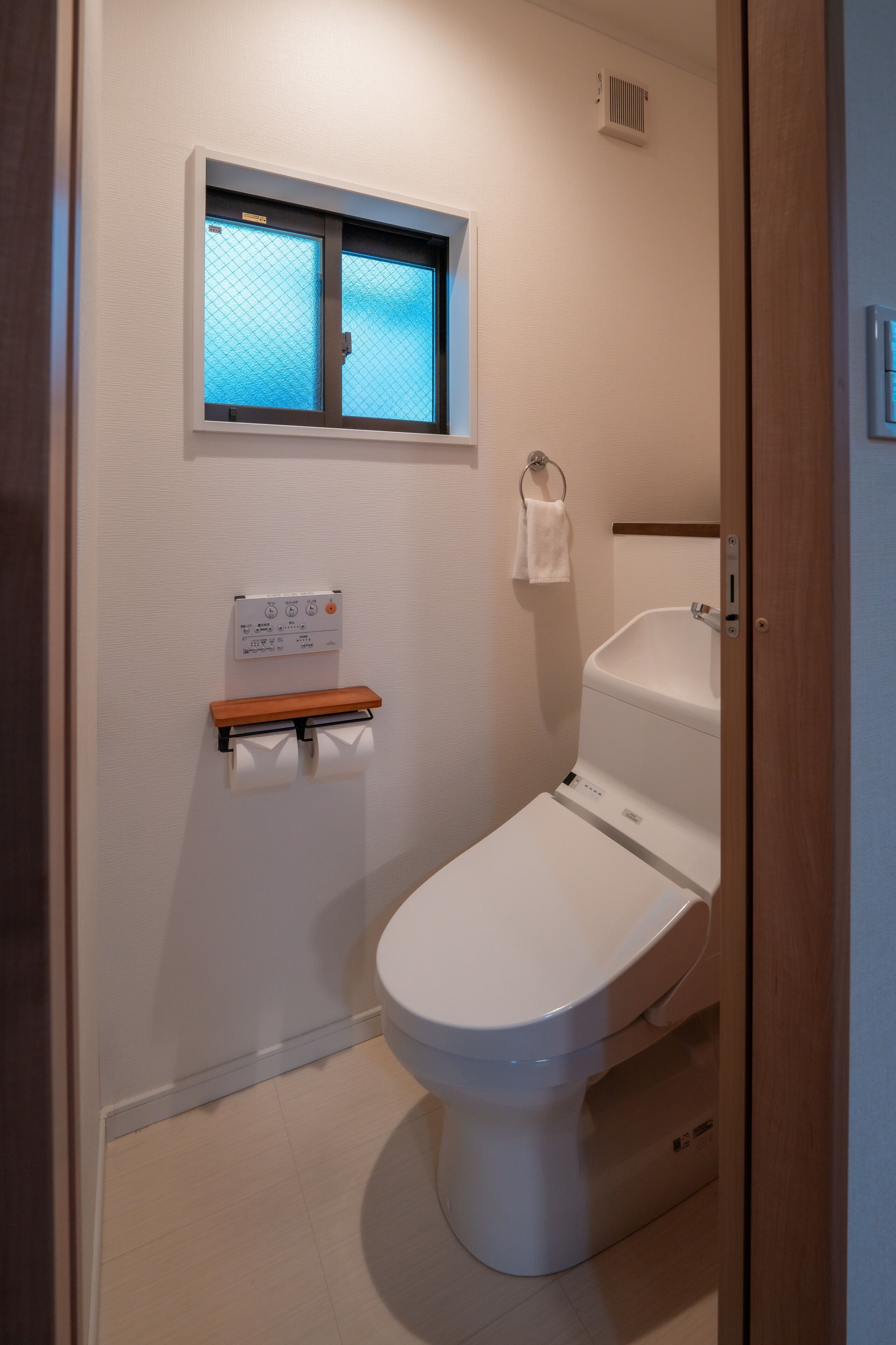 Et lille badeværelse med toilet, et vindue, et håndklædestativ og et panel monteret på væggen.