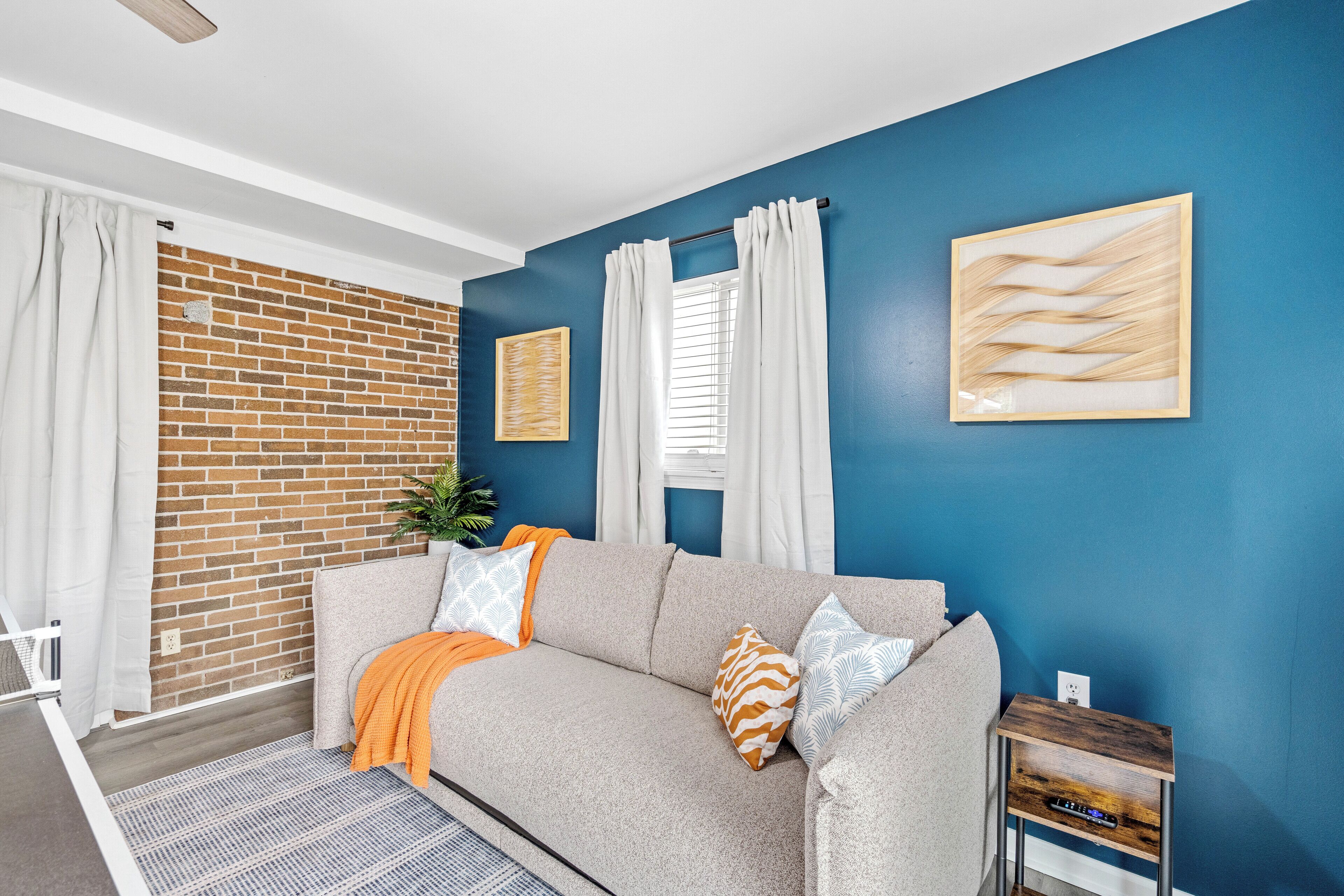 Un salon avec un mur en briques, un mur bleu, un canapé gris et une petite table d’appoint en bois.
