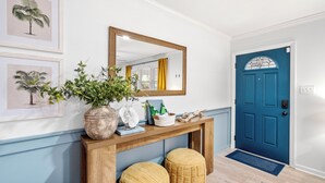 A hallway with a wooden console table, two wicker stools, a mirror, framed botanical prints, and a blue door. - 5RM2BA,Game Rm,FirePit,Golf,BBall,Near Parris Island (Beaufort)