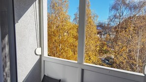 Un pequeño balcón con mesa y sillas, vista a árboles otoñales y suelo de baldosas de piedra.