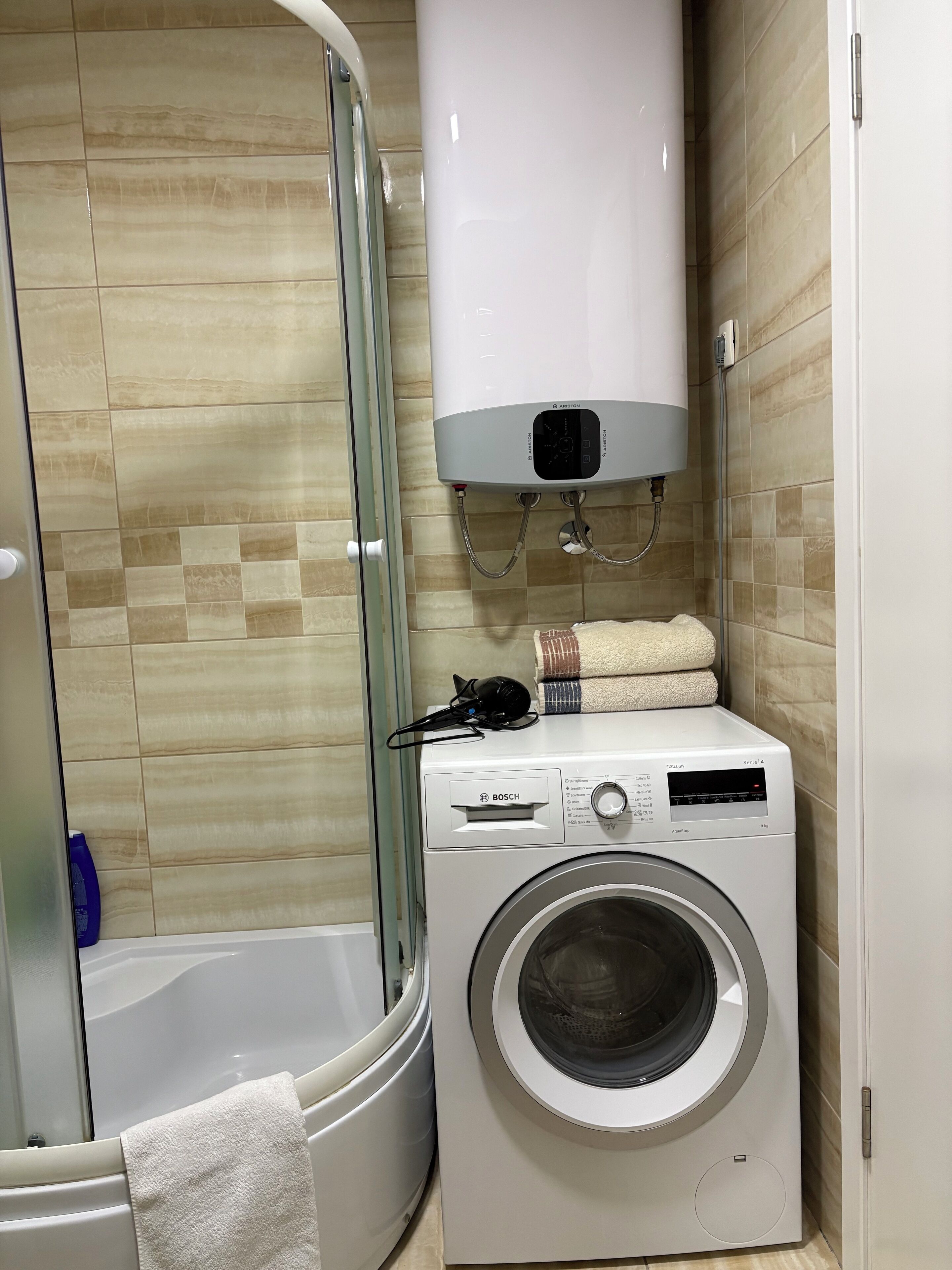 A compact bathroom with a built-in washing machine, a shower, and a toilet.