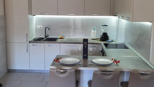 Una cocina moderna con armarios blancos, encimera de acero inoxidable y una barra con taburetes.