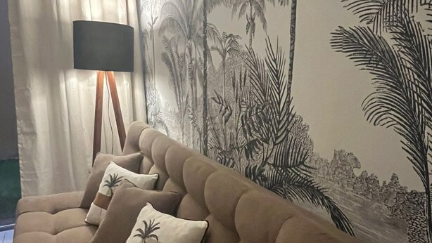 A living room with a brown sofa, two decorative pillows, a floor lamp, and a wall with a tropical wallpaper. - Vacation Rental for Carnival - Furnished Apartment" "Carnival 2026 (salvador)