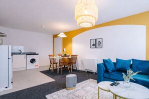 Ein kompakter Wohnbereich mit Essplatz, Küchenzeile und einem blauen Sofa.