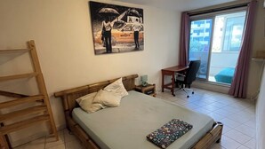 A bedroom with a wooden bed, a small desk, a chair, a painting on the wall, and a window with curtains. - Quiet, functional apartment - ideal for couples/families (Saint-Paul)