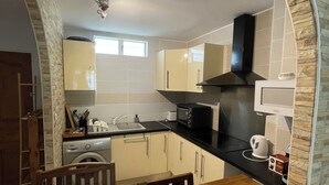 A compact kitchen with a stone archway, a washing machine, a microwave, and a kettle on the counter. - Quiet, functional apartment - ideal for couples/families (Saint-Paul)