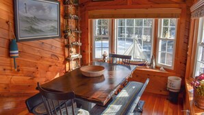 Un interior de madera con una mesa de comedor, sillas, un banco, una ventana con vistas al exterior y decoración temática náutica.