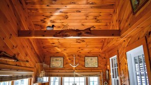 Interior de una cabaña con paredes y techo de madera, una araña, certificados enmarcados y una gran decoración de pez.