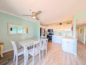 A modern kitchen with white cabinetry, a dining area with a glass table, and a ceiling fan. - Myrtle Beach Resort B0338 (Myrtle Beach)