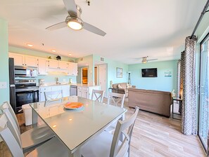 A modern kitchen with white cabinets, a dining table with chairs, a ceiling fan, and a living area with a sofa and TV. - Myrtle Beach Resort B0338 (Myrtle Beach)