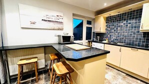 A modern kitchen with a central island, bar stools, and a tiled backsplash. - Dogs Welcome Peaks Retreat · Views · 3BR · Sleep 5 (Matlock)