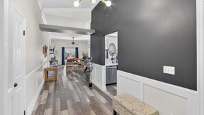 A spacious hallway with a wooden floor, a bench, and a kitchen area visible in the background. - Lakefront Home w/ Private Pool & Scenic Views (Brandon)