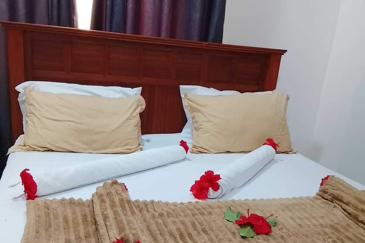 A bed with a wooden headboard, white linens, and a brown blanket with red flowers.