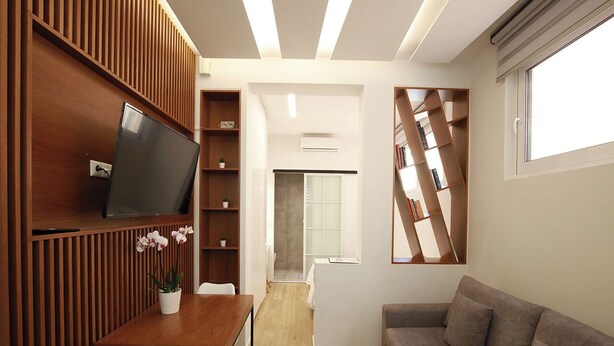 Ein modernes Wohnzimmer mit Holzwand, Flachbildfernseher, Esstisch mit Stühlen, Sofa und Bücherregal.