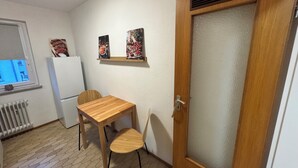 Una pequeña cocina con una mesa y sillas de madera, un refrigerador y dos cuadros colgados en la pared.