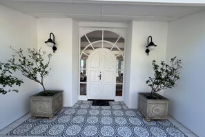A white entrance with a tiled floor, two potted plants, and a white door with a glass panel. - Luxury Tamboerskloof stay: panoramic Table Mountain views + secure parking (Cape Town)