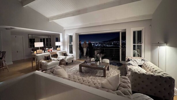 Uma sala de estar ampla com um sofá seccional grande, uma mesa de centro e vista para a cidade à noite.