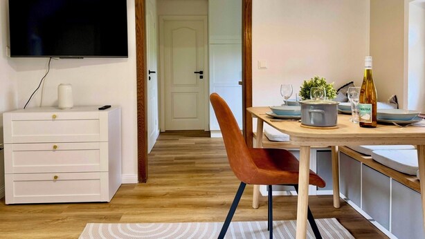 Et moderne køkken med spisebord, stole, et fjernsyn monteret på væggen og et træloft.