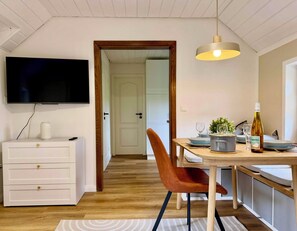 A modern kitchen with a dining table, chairs, a TV mounted on the wall, and a wooden ceiling.