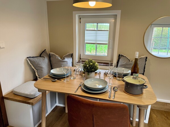 A dining area with a wooden table set for four, a potted plant, and a wine bottle.