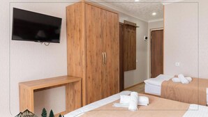 Habitació d'hotel amb un armari de fusta, un televisor penjat a la paret i dos llits amb tovalloles.