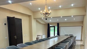 Una sala de conferències amb una taula de fusta llarga, cadires blaves, un lampadari i una pantalla de projector.