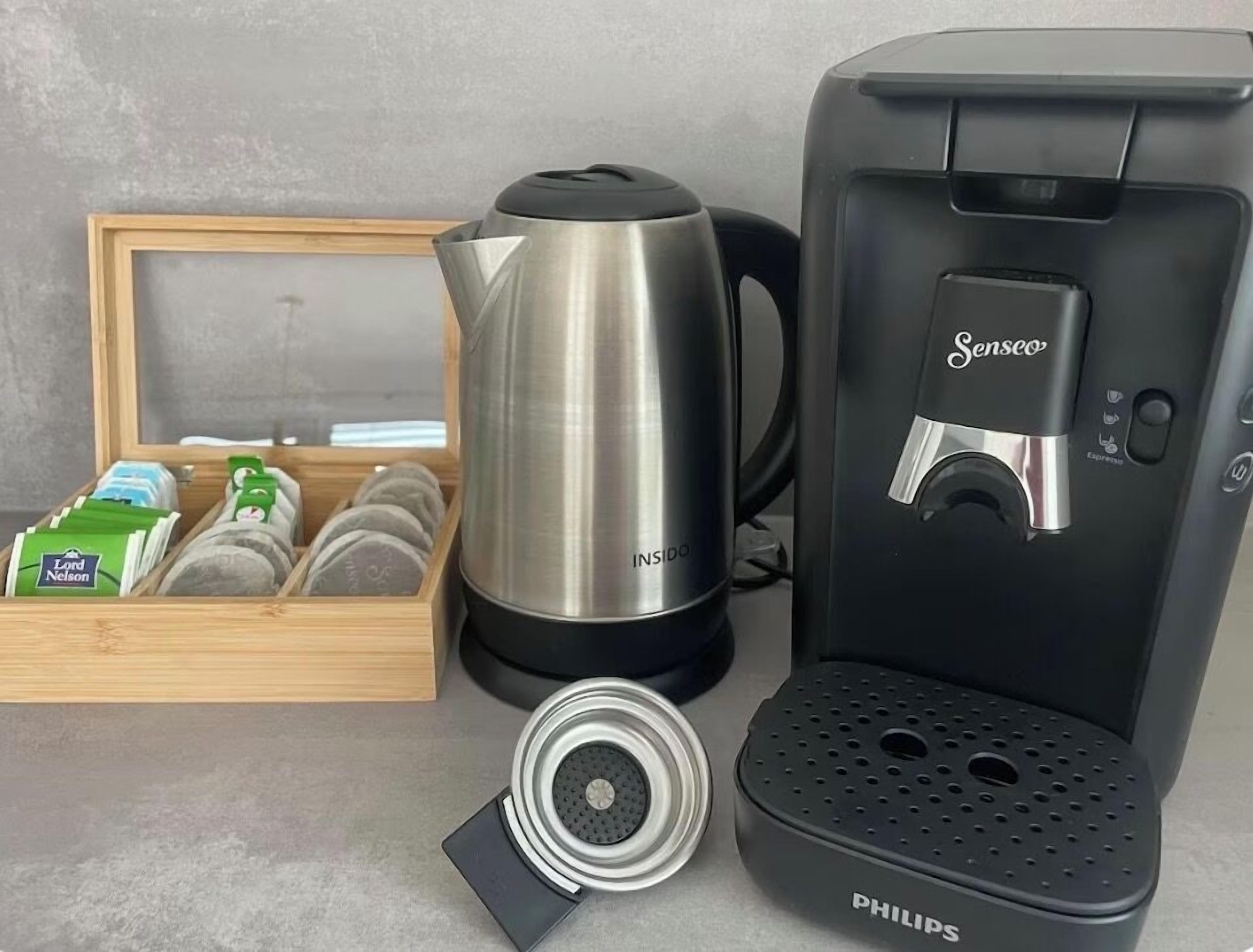 Una cafetera, un hervidor, una caja de cápsulas de café y un molinillo de café.