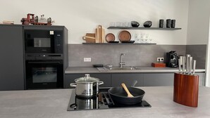 Een moderne keuken met een inbouwoven, magnetron en kookplaat. Boven het aanrecht staan planken met servies en glazen.
