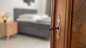 Een houten deur met een sierlijk metalen handvat, die leidt naar een slaapkamer met een bed en nachtkastje.